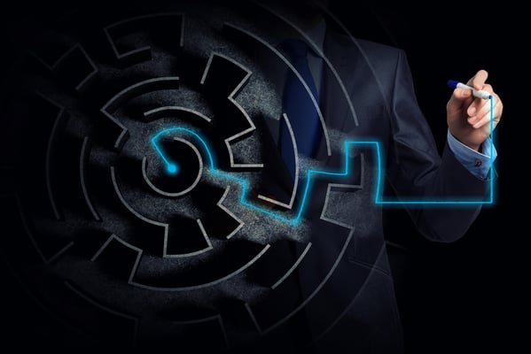 Male in business attire behind a top view of a maze with a blue marker tracing the exit.