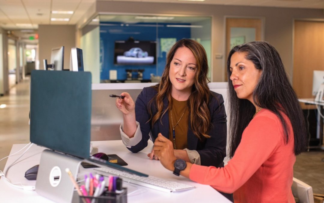 Two woman sitting at desk looking at computer