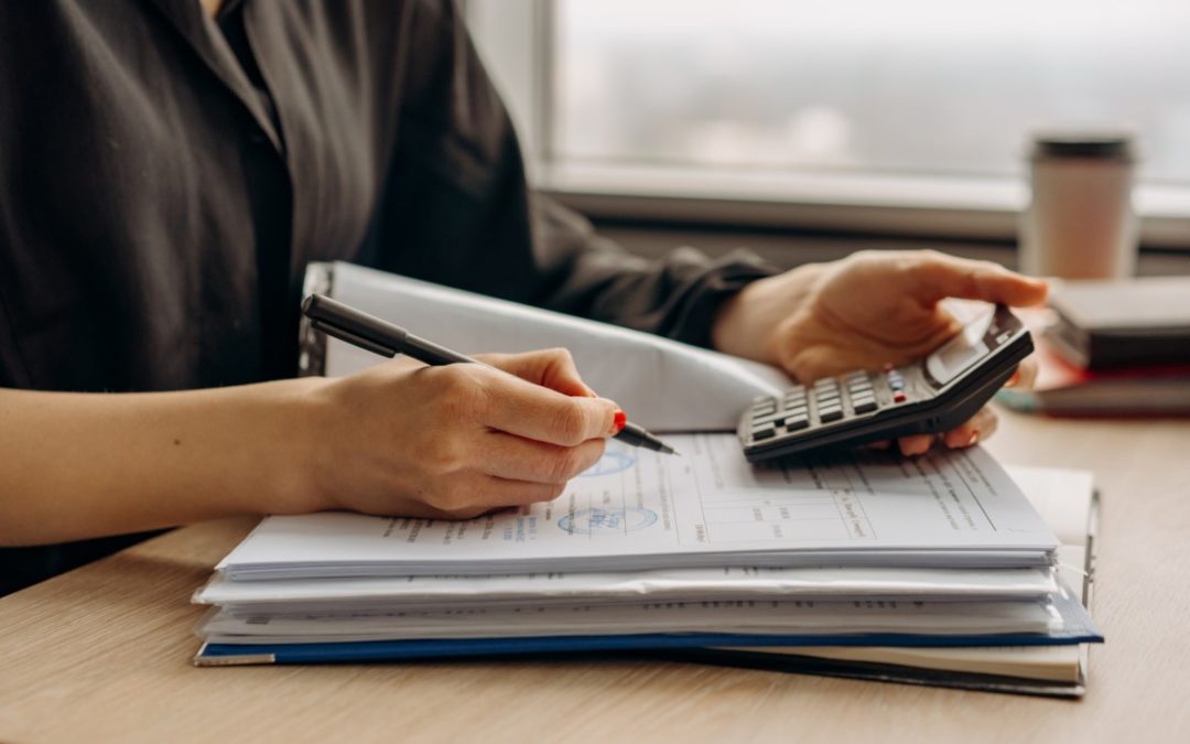 Person holding pen and calculator in hands on top of notebook