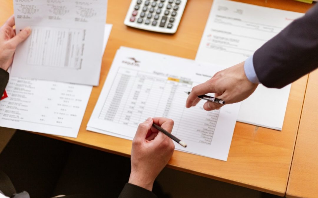 Two hands holding pencils pointing at paper on a desk